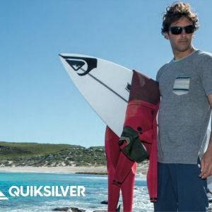 Quicksilver Brillen - Ein Mann mit Surfbrett steht mit einer Sonnenbrille am Strand.